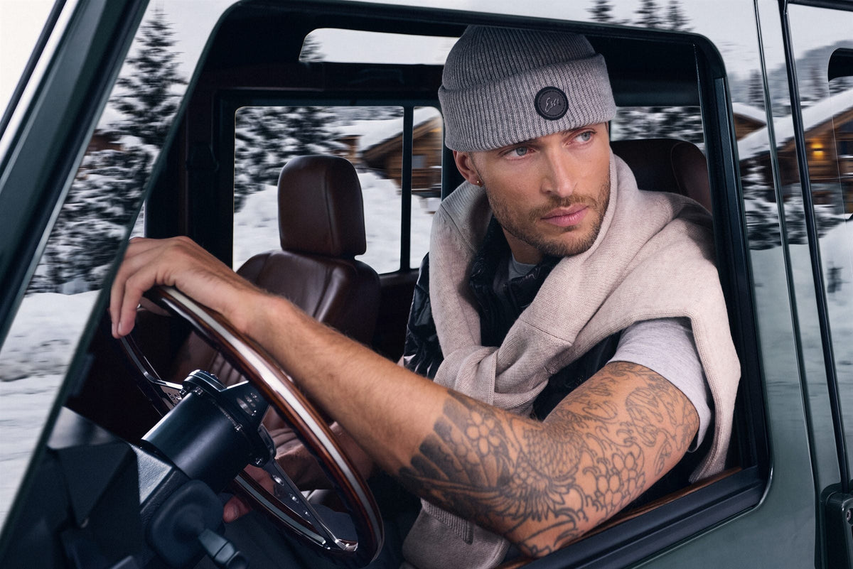 Man in a Grey Teton Beanie driving a vintage truck through a snowy village