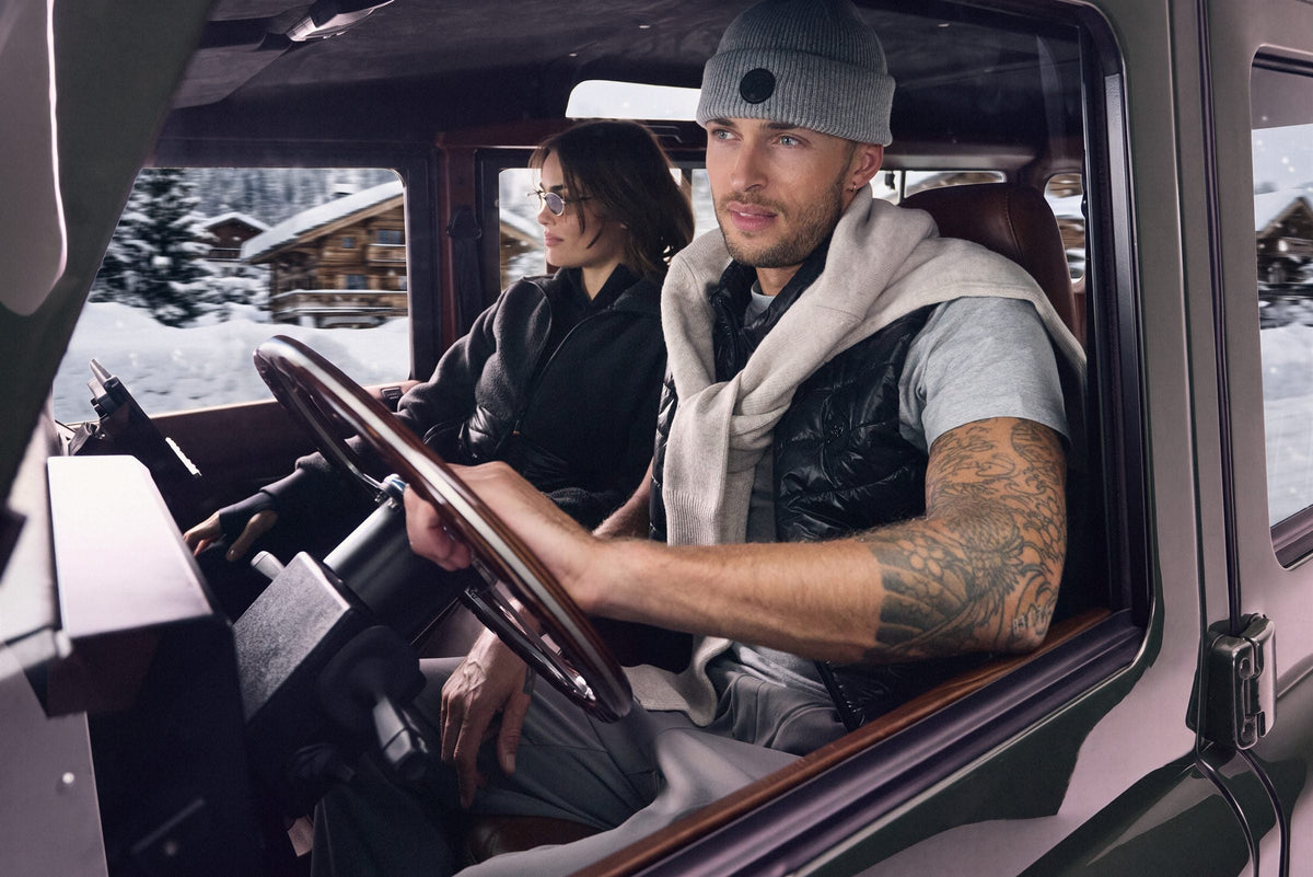 Man in a Grey Teton Beanie and black Vanguard Vest at the wheel of a vintage truck, snow outside